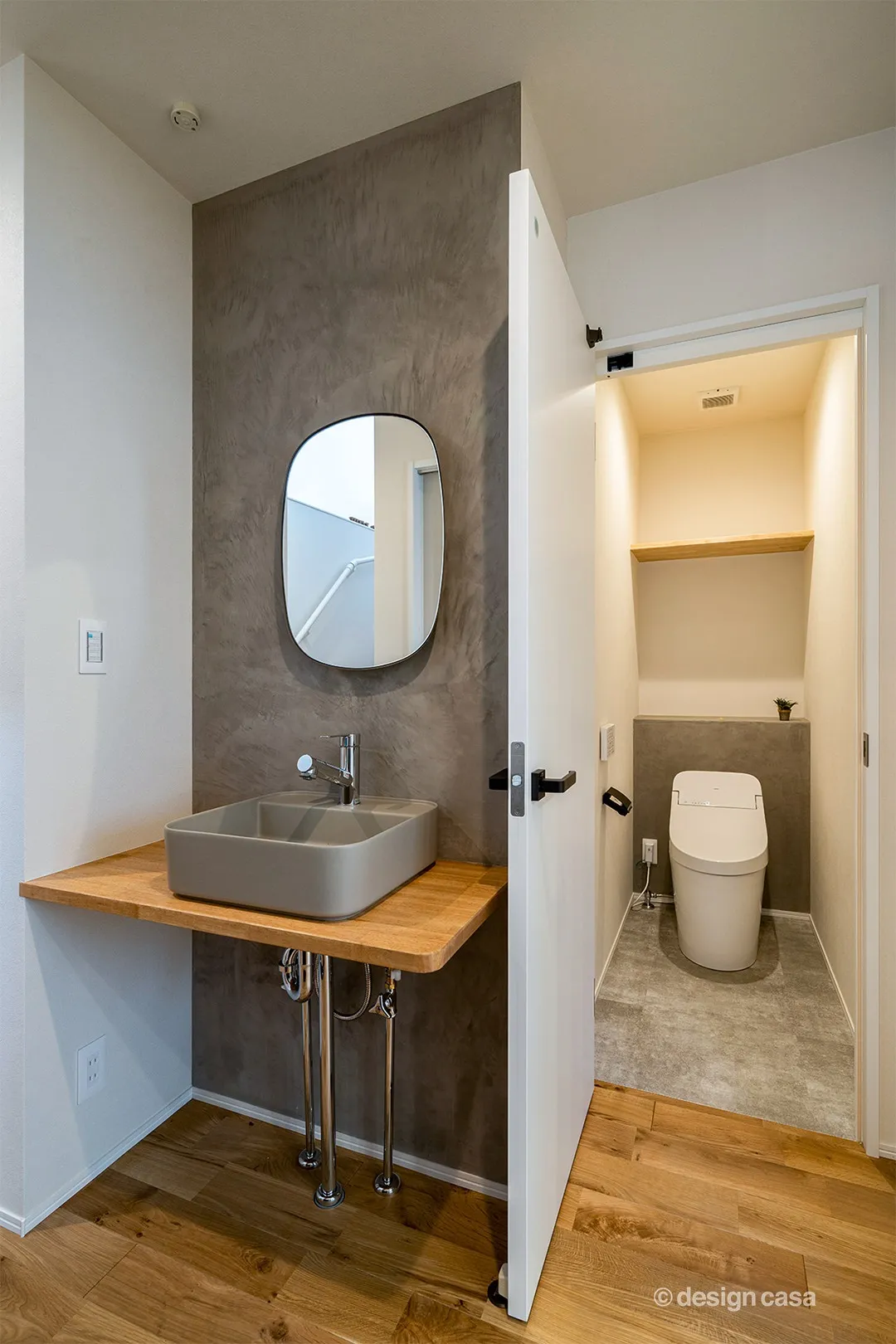 モルタル調のアクセント壁と丸みを帯びたブラックフレームのミラーがスマートな印象の１階洗面コーナー